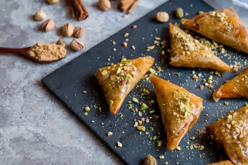 A plate of moroccan dessert topped with assorted nuts, showcasing its rich layers and golden-brown color.