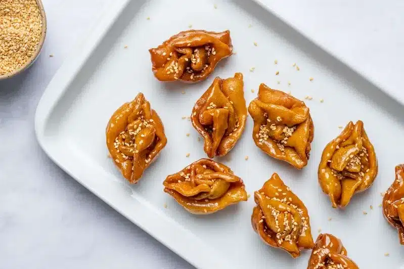 A plate of halwa chebakia and sour pork dumplings, beautifully arranged, showcasing their golden-brown exterior and vibrant sauce.