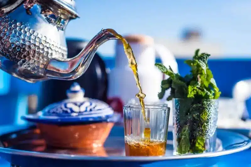 At a Moroccan luxury hotel, a person pours fragrant tea into a glass filled with fresh mint leaves.