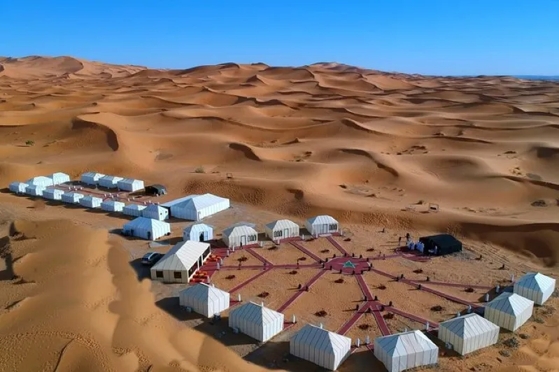 A group of tents set against sand dunes in the desert, showcasing a serene scene from a Merzouga camel ride experience.