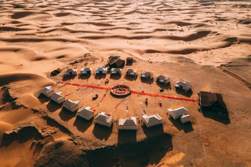 Aerial view of a desert camp in Merzouga, featuring a red circle, with camels nearby for riding.