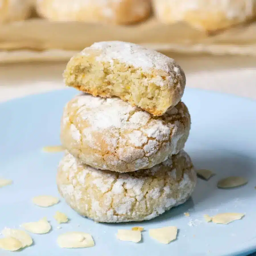 Three almond ghriba cookies stacked on a blue plate, showcasing their delightful texture and inviting appearance.