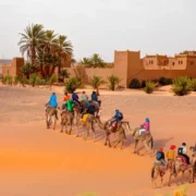 A group of people enjoying a camel ride in the desert landscape of Merzouga, surrounded by sand dunes.