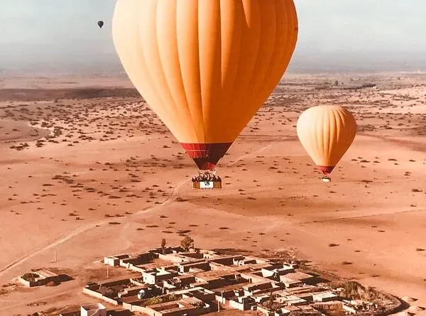 A colorful hot air balloon soaring over the desert landscape of Marrakech, with clear blue skies in the background.
