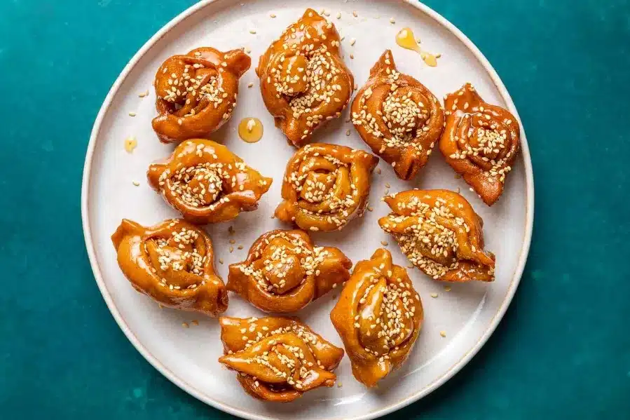 A plate featuring cinnamon rolls garnished with sesame seeds, alongside traditional halwa chebakia.