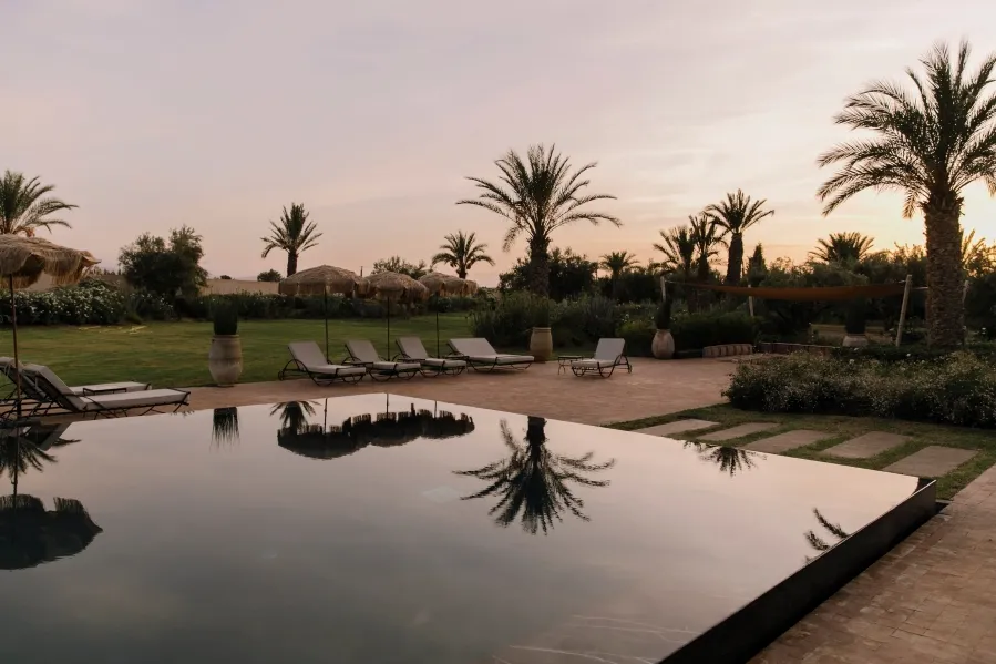 A serene pool encircled by lush palm trees and green grass, ideal for yoga retreats in Marrakech.