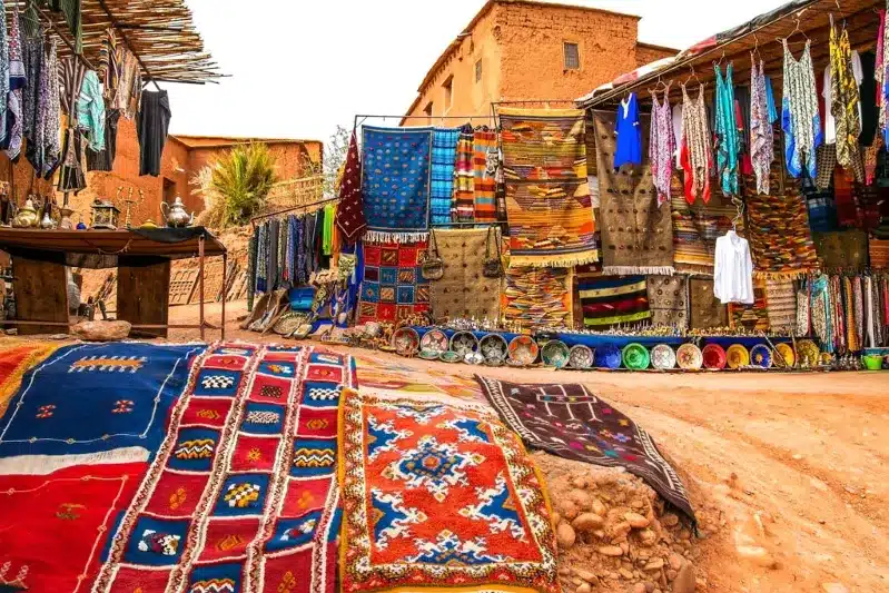 A vibrant Marrakech market showcasing colorful rugs and clothing, highlighting local craftsmanship and culture. 