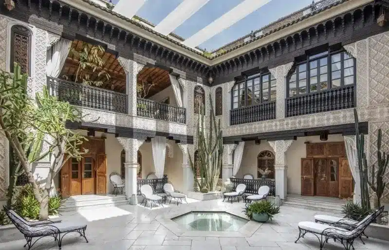 A serene courtyard of an old Moroccan house featuring a tranquil pool surrounded by lush greenery. 