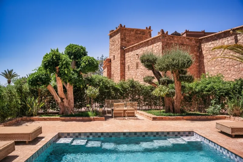 A serene pool in front of a large building, featuring a central tree, ideal for a relaxing Morocco vacation.