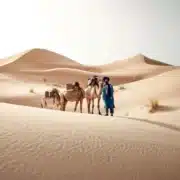 A man stands beside his camels in the Moroccan desert, showcasing a travel experience with a local travel agent.