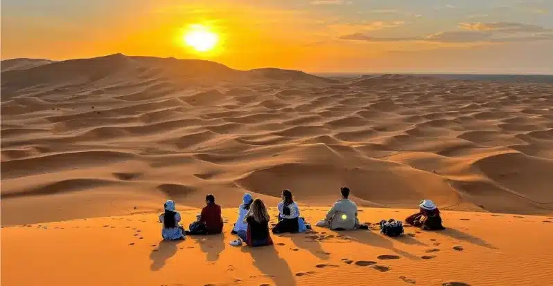 People silhouetted against a vibrant sunset in the Sahara Desert, showcasing the beauty of Morocco's landscapes. 