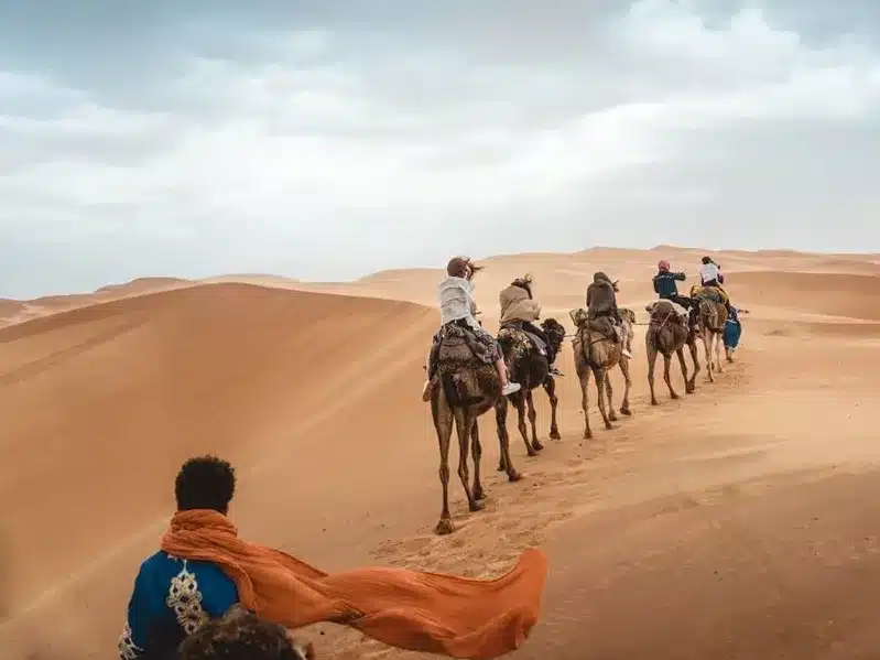 People riding camels across the vast Sahara Desert, showcasing a unique experience offered by Casablanca Morocco Tours.
