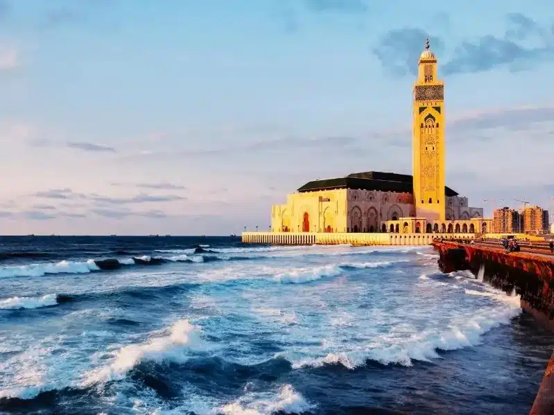 A large building with a clock tower beside the ocean, representing Casablanca, Morocco Tours.
