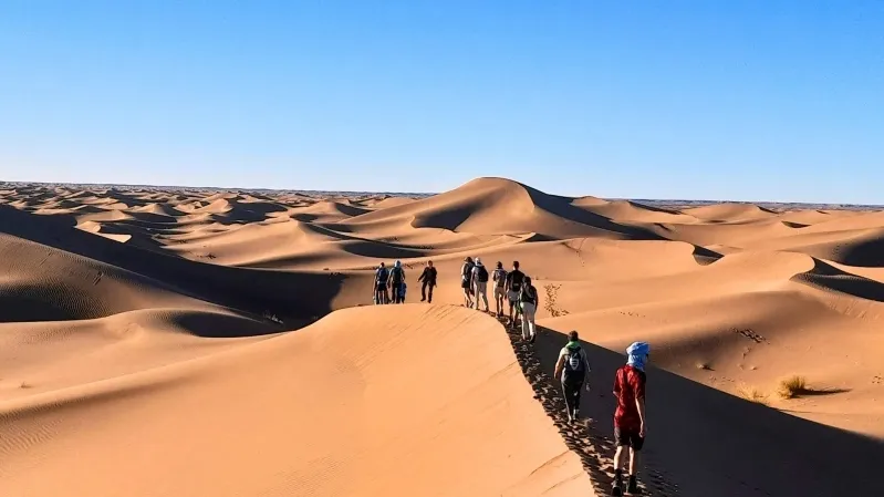 People walking across a sand dune in the Sahara Desert during a Fes to Marrakech desert tour.