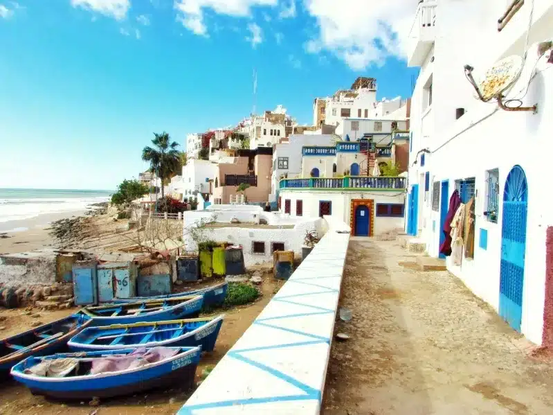 A scenic beach in Morocco featuring boats and buildings along the shore, inviting visitors without visa requirements.