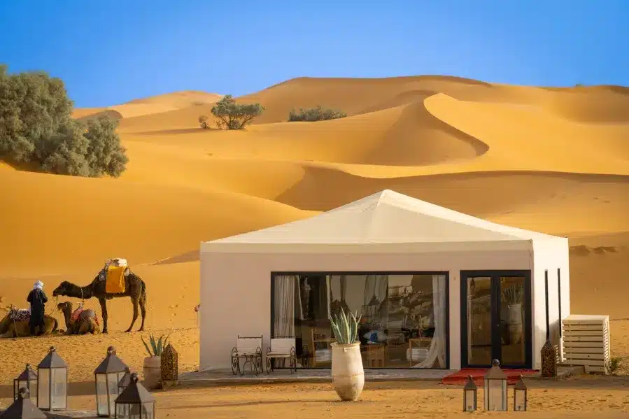 A desert scene featuring a tent, camels, and people, highlighting the Fes to Marrakech desert tour experience.