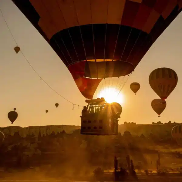 Hot air balloons soar over a desert landscape at sunset, with vibrant colors illuminating the sky. Air Morocco Safety.