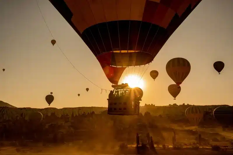 Hot air balloons soar over a desert landscape at sunset, with vibrant colors illuminating the sky. Air Morocco Safety.