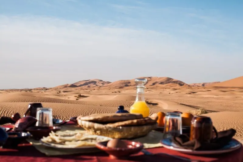 Breakfast spread in a Moroccan desert setting, featuring traditional dishes and vibrant colors, Morocco tour from America.

