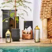 A serene courtyard pool surrounded by a brick wall and a large tree, evoking a Moroccan dream atmosphere.