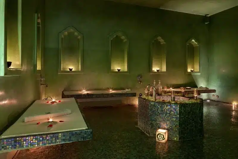 A serene spa room featuring lit candles and a calming green wall, highlighting unique Moroccan relaxation experiences.

