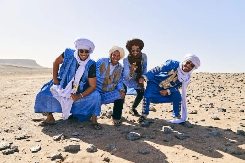 Four men dressed in traditional attire pose in the desert, reflecting the rich Morocco lifestyle and culture.
