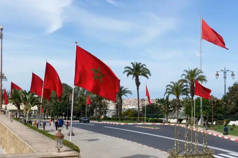 A collection of red flags, including the Moroccan flag, fluttering in the air against a clear blue sky.