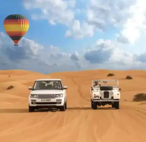 Two vehicles drive through a desert landscape, with a colorful hot air balloon floating in the background, showcasing Morocco tours.