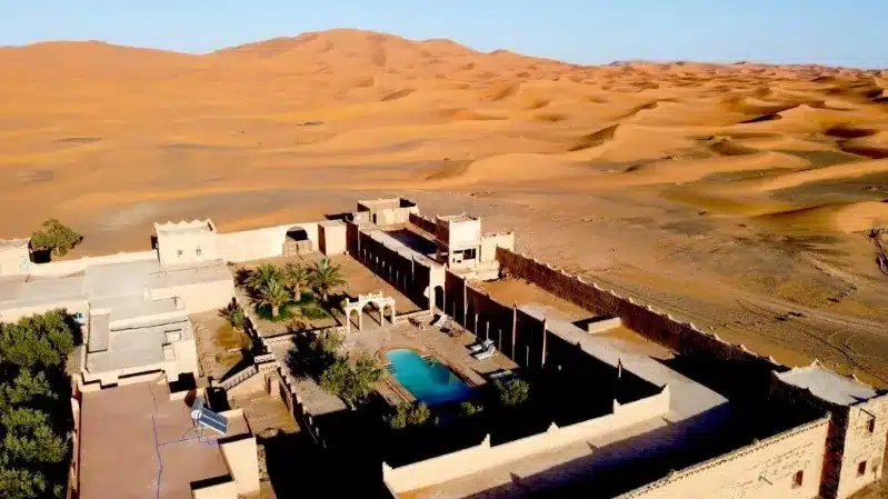 A desert house with a pool surrounded by sand, showcasing a serene oasis in the Moroccan desert landscape.