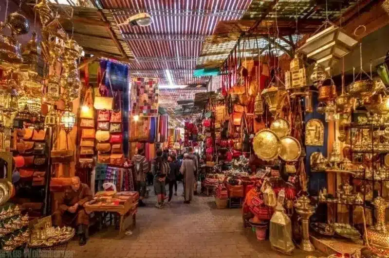 A bustling Marrakesh market filled with colorful stalls, vibrant textiles, and shoppers exploring local goods and spices.