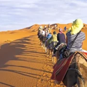 People riding camels across a vast desert landscape, showcasing a unique travel experience in Morocco.