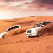 Two SUVs driving through the Moroccan desert at sunset, showcasing a vibrant sky and sandy landscape.