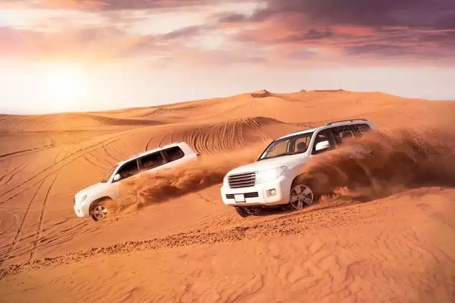 Two SUVs driving through the Moroccan desert at sunset, showcasing a vibrant sky and sandy landscape.