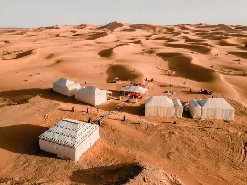 A desert camp in Morocco featuring several tents and a large white canopy under a clear blue sky.