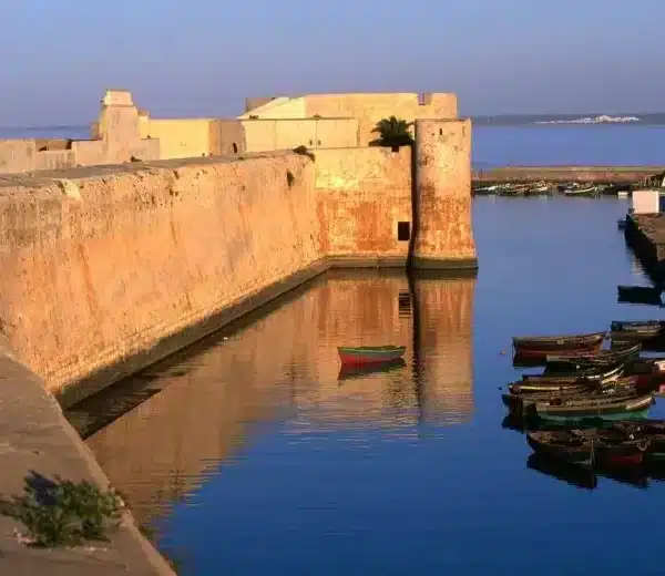 Boats are docked in a canal beside an ancient wall during a day trip to El Jadida.