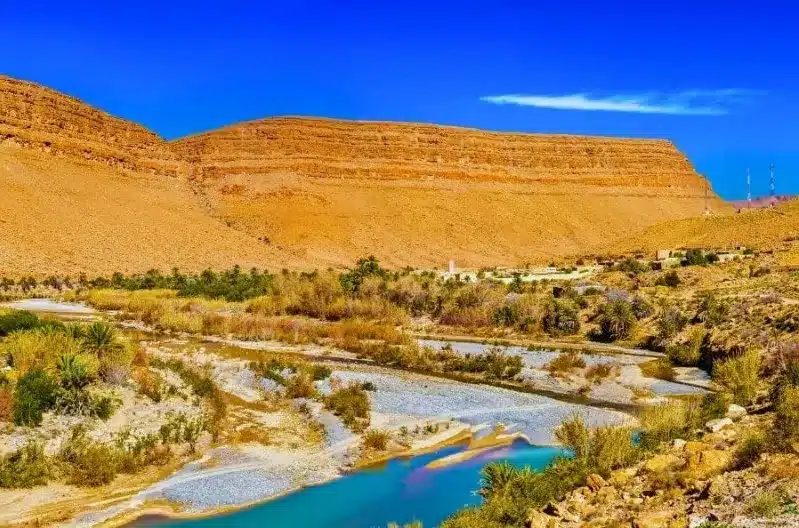 A serene river flowing through the arid landscape of Morocco's Ziz Valley, showcasing the contrast of water and desert.