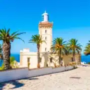 A scenic lighthouse on the coast surrounded by palm trees, representing Tangier Private Tours.