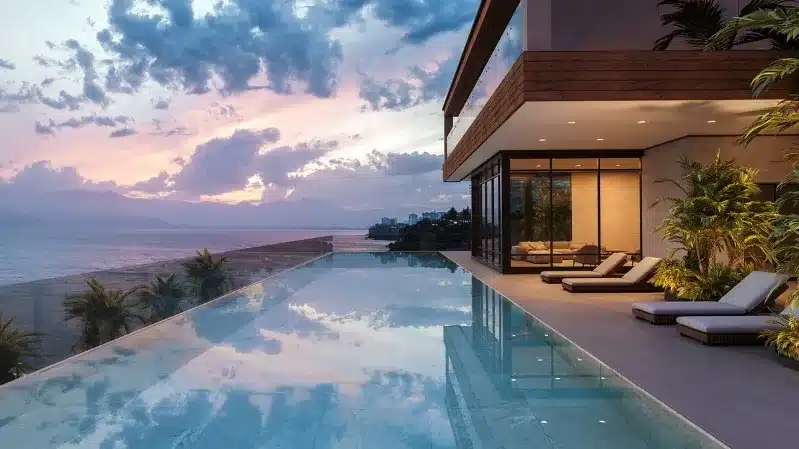 A luxury home with large windows overlooks the ocean at sunset, showcasing vibrant colors and serene coastal beauty.