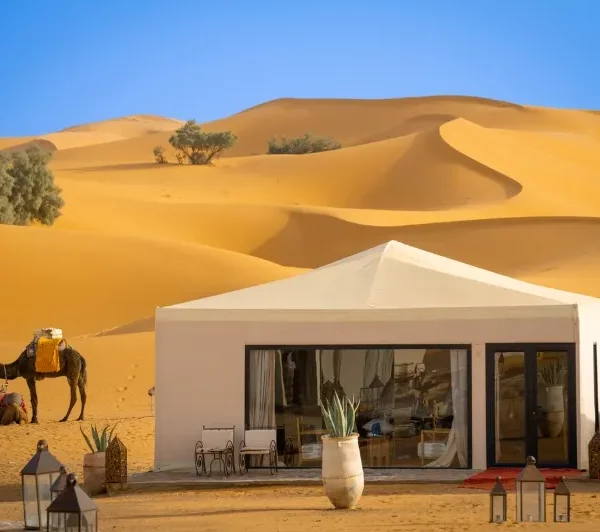 A desert scene featuring a tent, camels, and people, highlighting the 2 Days Fes to Merzouga Desert Tour experience.