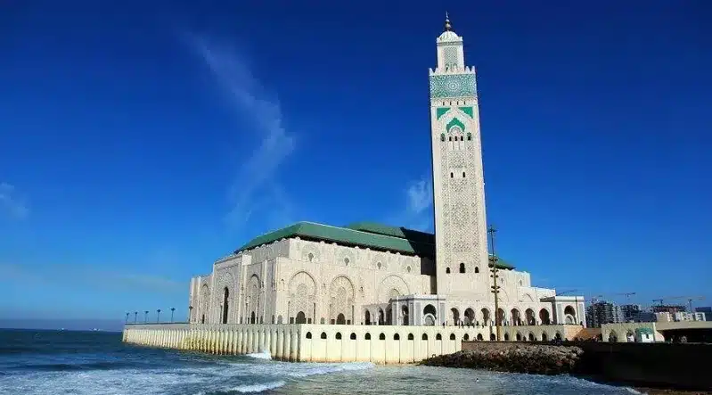 A mosque stands on the beach in Casablanca, overlooking the ocean, showcasing a blend of architecture and natural beauty.
