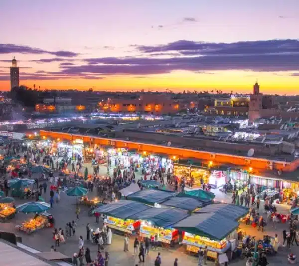 The city of Marrakesh at dusk, showcasing vibrant lights and silhouettes against a colorful sky.
