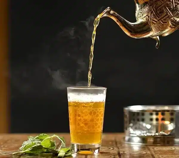 A tea kettle pouring tea into a glass during a traditional Moroccan tea ceremony.