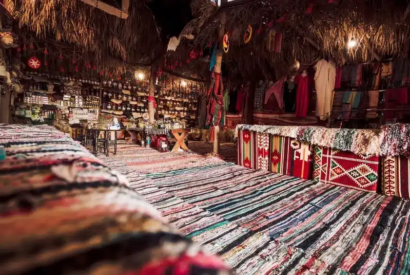A quaint rug shop nestled in a village, showcasing colorful rugs, surrounded by traditional architecture.
