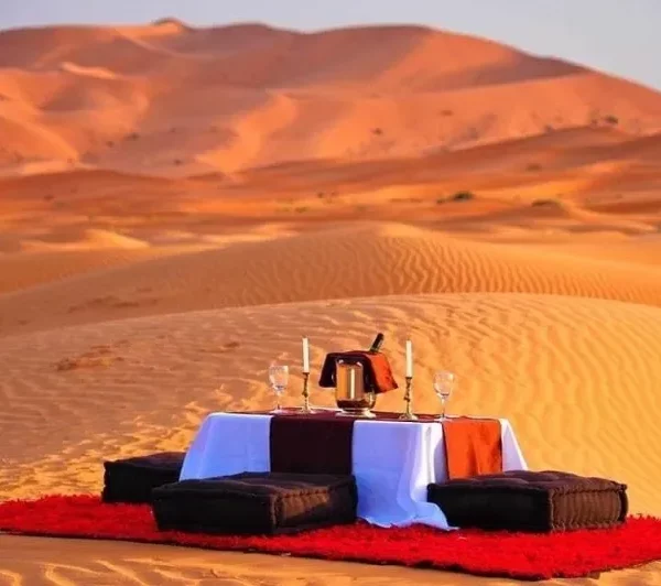 A romantic desert scene featuring a table and two chairs, set for an intimate dinner under the stars.