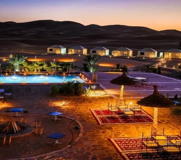 Sunset over a desert pool with a tent and lounge chairs, highlighting a serene moment during a 9-day tour from Marrakech.