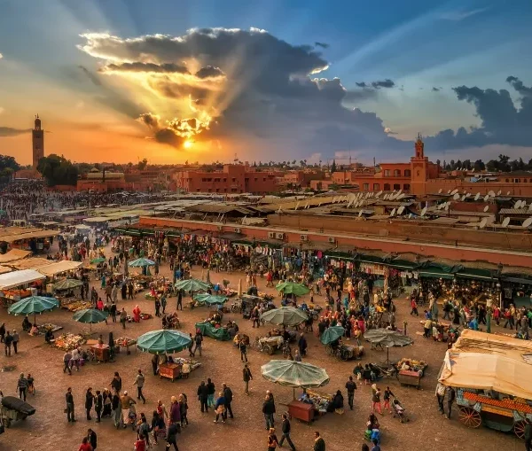 Sunset casts a warm glow over the bustling market in Marrakech, highlighting the vibrant colors and lively atmosphere.