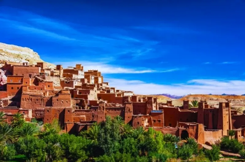 A panoramic view of a Moroccan city nestled in the desert, showcasing traditional architecture against a sandy landscape.