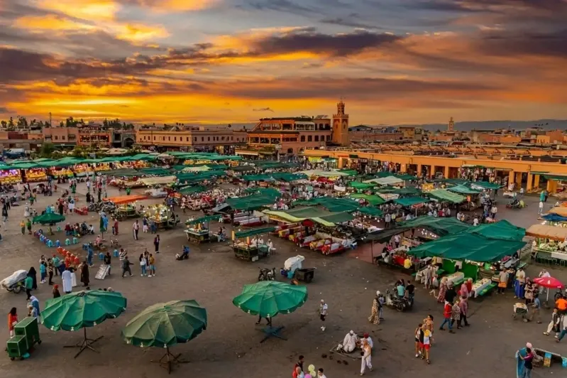 Sunset casts warm hues over the bustling market in Marrakech, highlighting the vibrant atmosphere of Morocco.