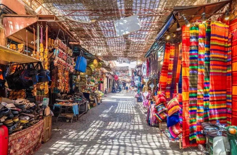 A narrow street lined with vibrant cloths and bags, showcasing a lively atmosphere, ideal for family travel adventures.