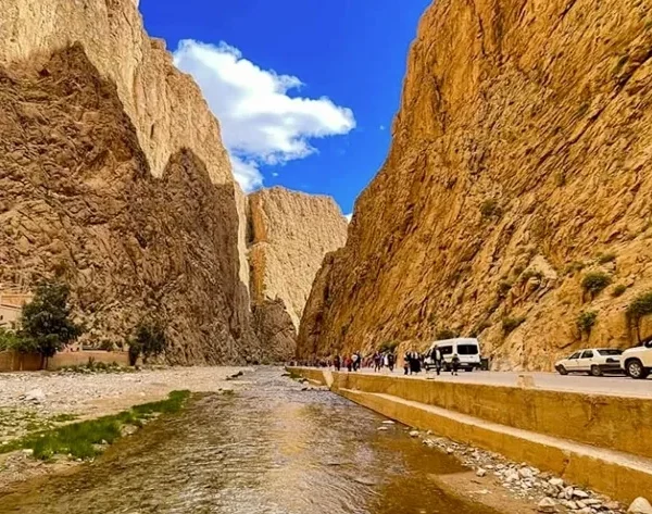 A river flows through a canyon surrounded by mountains, showcasing the natural beauty of the Ouarzazate to Fes route.